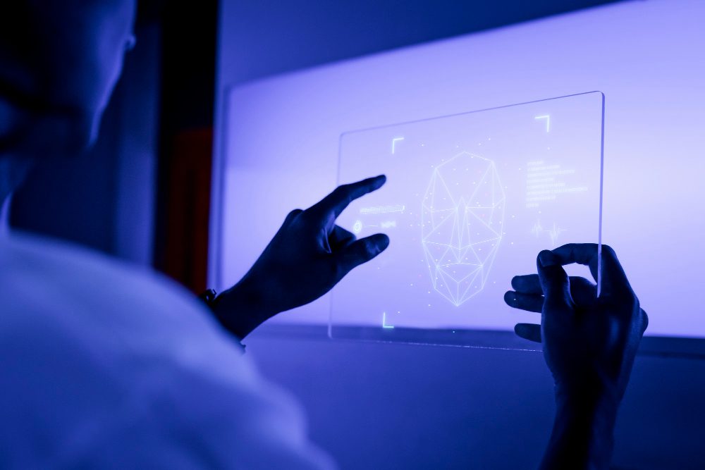 774985 - Zeta Nueve - Europa News 24h Person uses a transparent touchscreen to manipulate a holographic wireframe of a human head on a blue-lit display.