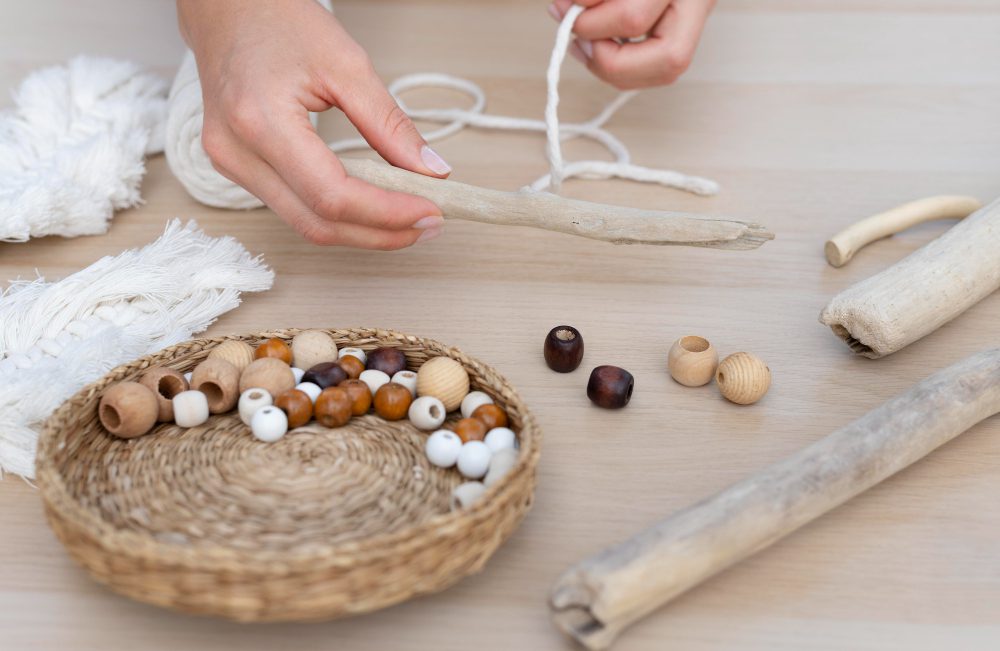 Close-up of hands threading a string through wooden beads over a basket of beads on a craft table.