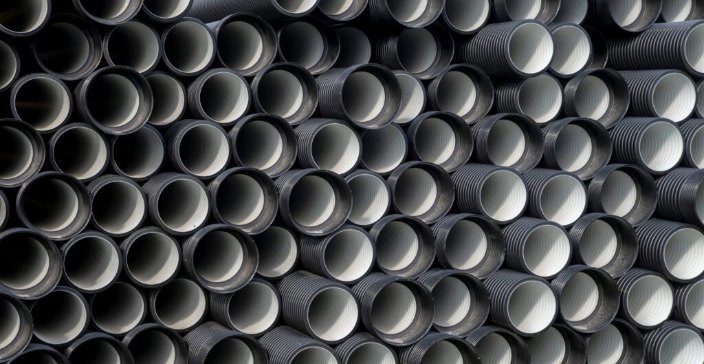 Close-up of stacked dark gray corrugated plastic pipes with white interiors.