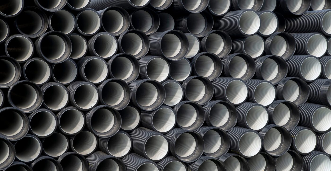 Warehouse of black plastic water pipes in outdoor storage site - Europa News 24h Close-up of stacked dark gray corrugated plastic pipes with white interiors.