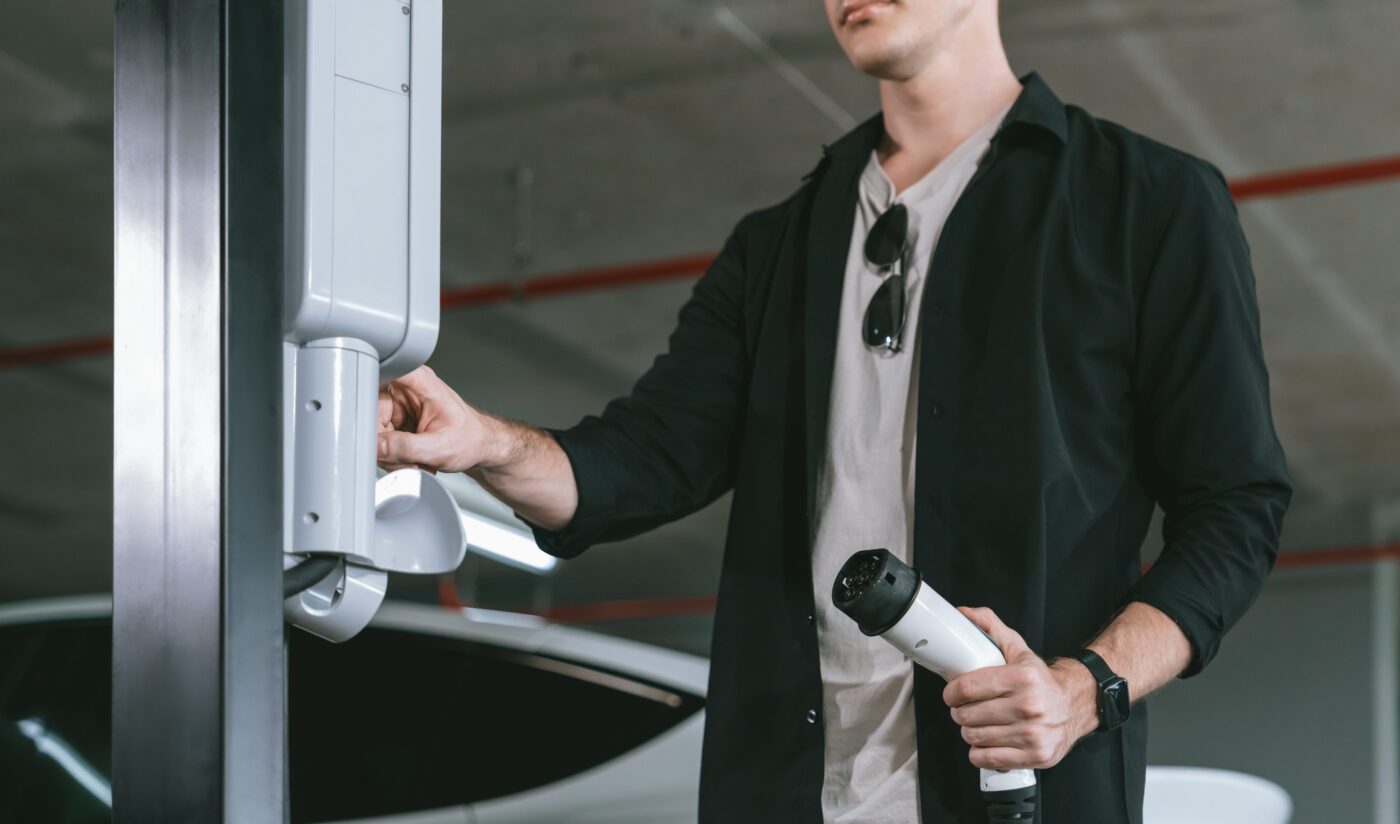 775544 Moveclean - Europa News 24h Man connects an electric vehicle charging cable to a wall unit beside a parked car in a garage.