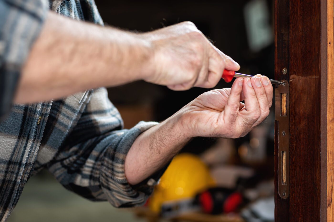 Cerrajeros metropolitano - IP - Europa News 24h Close-up of a person in a plaid shirt using a screwdriver to install a door latch in a wooden door.