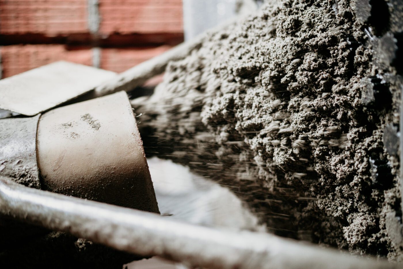 Concrete is being poured from a chute onto a brick wall, forming wet cement at a construction site.