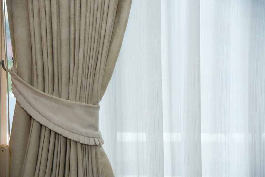 Beige drapes tied back to reveal sheer white curtains at a window.