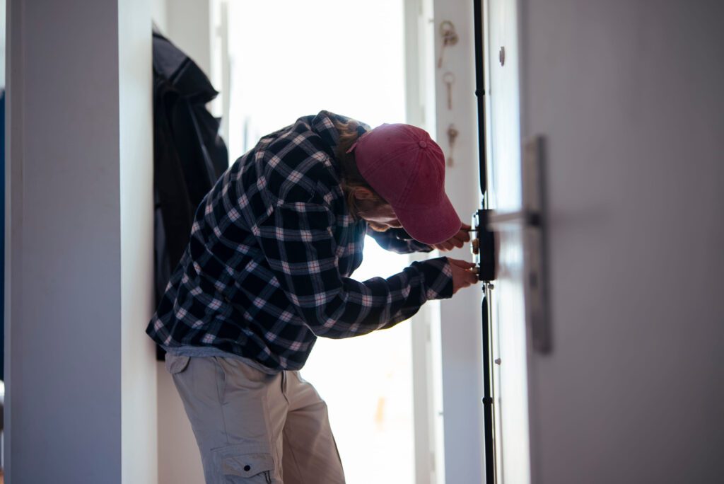 Person in a red cap and plaid shirt locking a door in a narrow hallway.