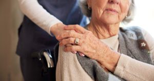 Caregiver's hand rests on an elderly woman's shoulder, conveying comfort and support.