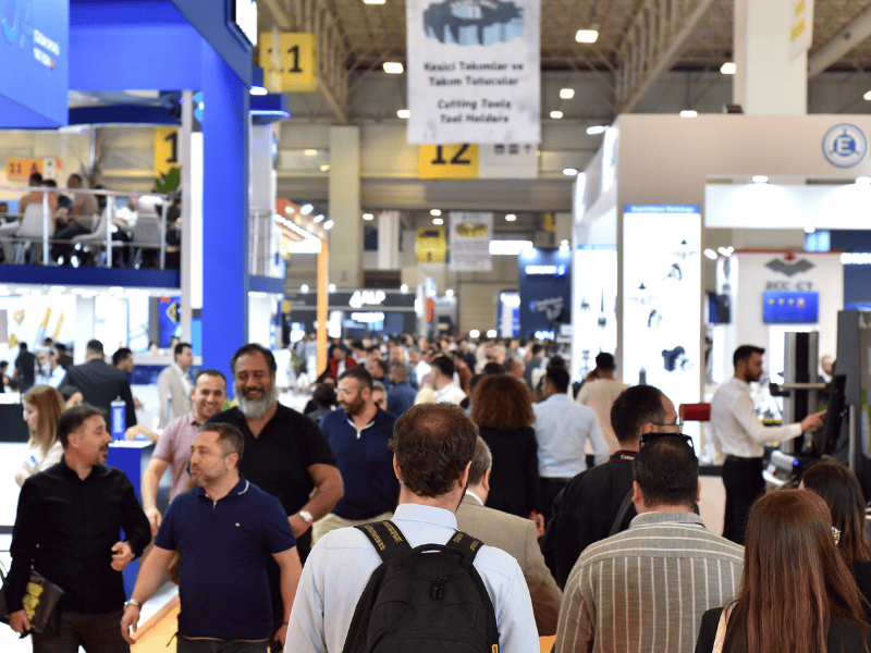 Busy trade show hall with people wandering between exhibitor booths and hanging banners (numbers 11 and 12)