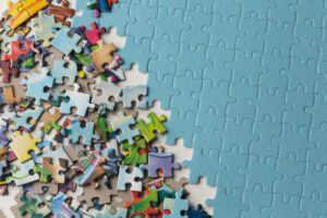 Assorted colorful jigsaw puzzle pieces spread across a blue puzzle surface, as if waiting to be assembled.