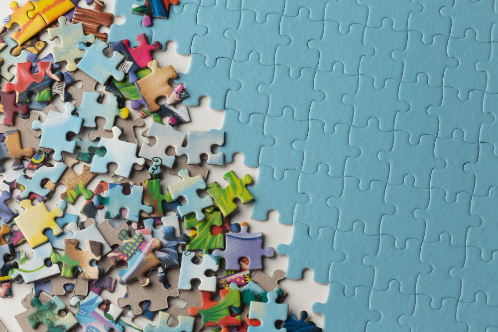 784011 - Tallers Guinardó - Europa News 24h Assorted colorful jigsaw puzzle pieces spread across a blue puzzle surface, as if waiting to be assembled.