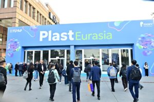 Crowd of people walking toward the glass doors of a blue Plast Eurasia expo entrance.