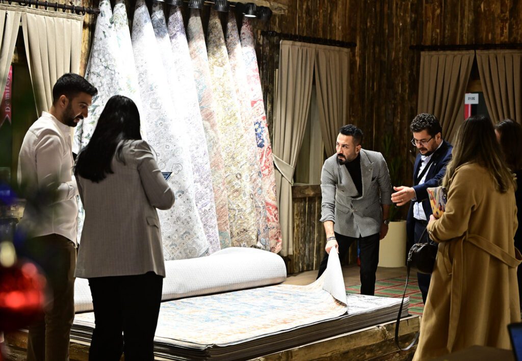 Group of people inspecting rolled and hanging carpets in a rug showroom.